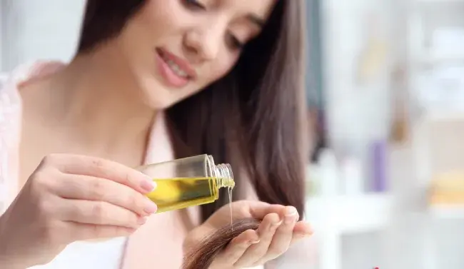 زنی در حال استفاده از روغن کرچک گیاهی روی موهایش