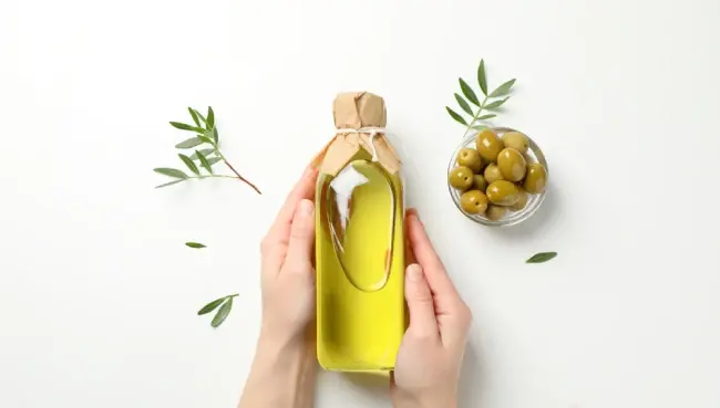 فردی روغن زیتون را در کنار پیاله‌ای پر از زیتون در دست گرفته