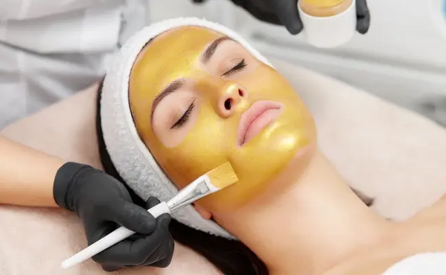 متخصص در حال زدن ماسک طلا روی صورت یک زن