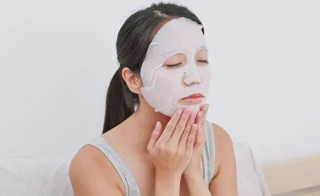 زنی در حال استفاده از ماسک ورقه ای روی صورت خود